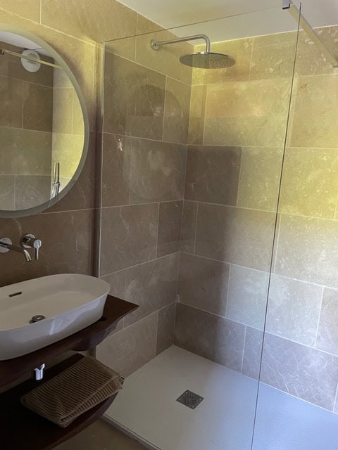 Modernes Badezimmer mit Natursteinfliesen, begehbarer Dusche, Spiegel und Waschbecken.